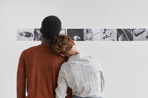 Achteraanzicht portret van gemengd ras paar omarmen tijdens het kijken naar schilderijen op moderne kunst galerie tentoonstelling,