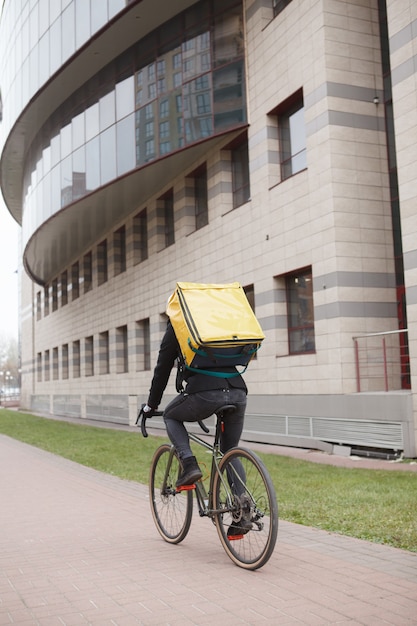 Achteraanzicht shot van een koerier thermo rugzak dragen, fietsen in de stad