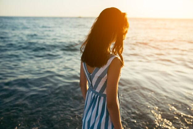 Achteraanzicht silhouet van portret brunette mooie vrouw wandelen langs strand en zee zonsondergang achtergrond Cover idee vrouw in jurk lopen op Oceaan kijken naar de zon Eenzaamheid en verdriet concept