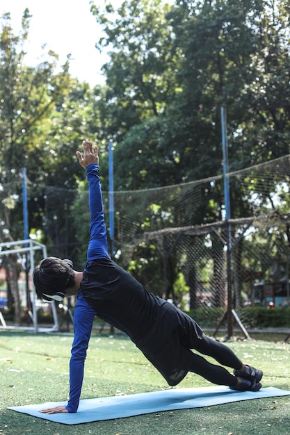 Achteraanzicht van aantrekkelijke gezonde jonge sportman die zich uitstrekt op fitnessmat buiten in het park