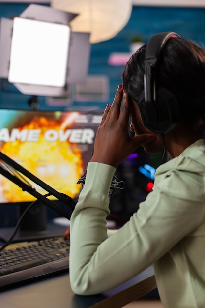 Achteraanzicht van afro-amerikaanse esport-streaming die virtuele concurrentie verliest met een koptelefoon. professionele gamer die online videogames streamt met nieuwe afbeeldingen op krachtige computer.