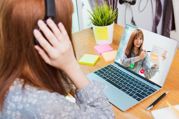 Achteraanzicht van Aziatische zakenvrouw slim werken vanuit huis met behulp van laptop online bellen naar gespreksplan in webcam videoconferentie onder avondklok quarantaine pandemie coronavirus COVID-19