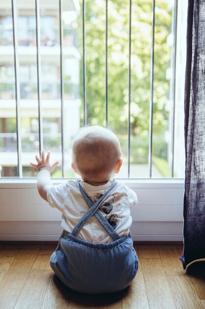 Achteraanzicht van babyjongen die door het raam kijkt
