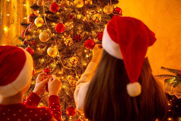 Achteraanzicht van broer en zus die de kerstboom versieren met kerstballen en lichten in de woonkamer Bereid decoraties voor om Kerstmis te vieren