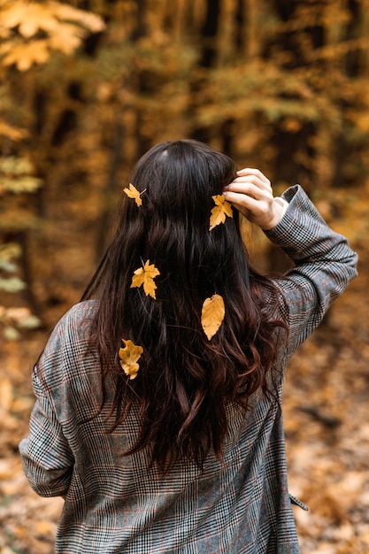 Achteraanzicht van brunette vrouw met herfst gele bladeren in lang haar op herfst natuur achtergrond