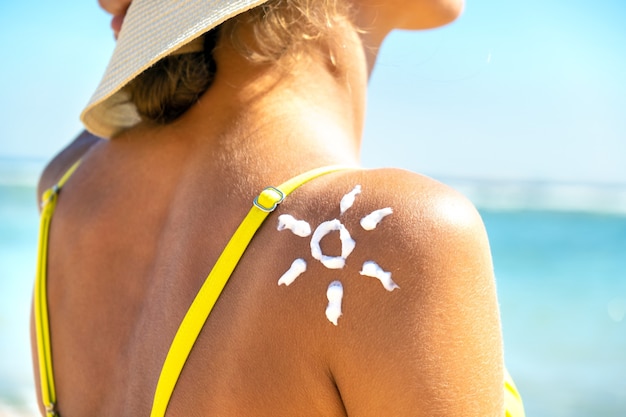 Achteraanzicht van de jonge vrouw die op het strand met zonnebrandcrème in zonvorm op haar schouder looien