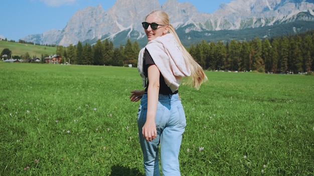 Achteraanzicht van de jonge vrouw die op het veld met bergen vooraan loopt