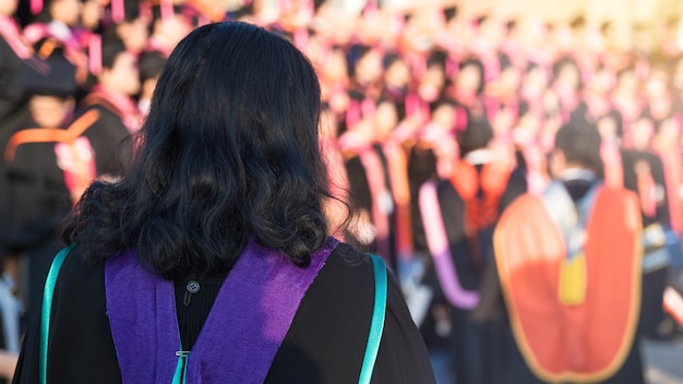 Achteraanzicht van de universitair afgestudeerden in de rij voor de graadprijs in de universitaire diploma-uitreiking. De universitair afgestudeerden verzamelen zich tijdens de universitaire diploma-uitreiking. Menigte van de afgestudeerden.