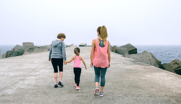 Achteraanzicht van drie vrouwelijke generaties die langs de zeepier lopen