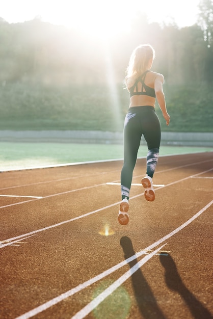 Achteraanzicht van een atletische vrouw die op het spoorstadion loopt in de zomerochtend, een lichte fitte vrouw die loopt