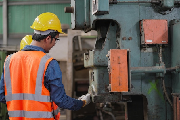 Achteraanzicht van een Aziatische ingenieur die een grote machine in een fabriek inspecteert om te repareren