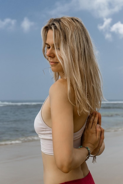 Achteraanzicht van een fitte gezichtsloze vrouw in activewear die aan de kust staat en meditatie beoefent terwijl ze yoga op het strand doet