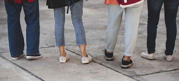 Foto achteraanzicht van een groep van vier jonge meisjes, studentenbenen en sneakers die samen op de universiteitscampus buiten staan. concept voor onderwijs, vriendschap en studentenleven.