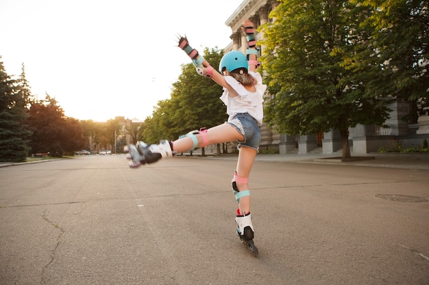 Foto achteraanzicht van een jong meisje met beschermende kleding voor skaten die op haar rolschaatsen danst