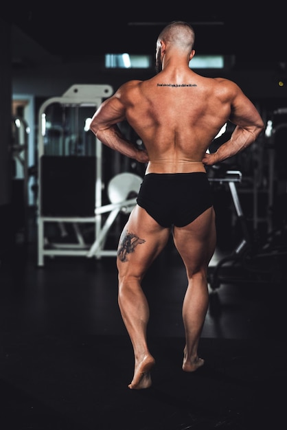 Achteraanzicht van een jonge gespierde bodybuilder die zijn perfecte rugspieren laat zien terwijl hij poseert na het sporten in de sportschool.