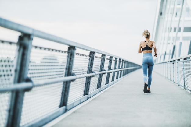 Achteraanzicht van een jonge gespierde vrouw die buiten traint. Ze rent op de brug in de stad.