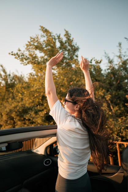 Achteraanzicht van een jonge vrouw die haar handen in de lucht steekt tijdens een roadtrip in een cabriolet concept van zorgeloze zomervakantie