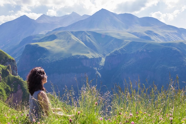 Achteraanzicht van een jonge vrouw die op de top van een berg zit en in de verte kijkt op de top van de berg Achtergrond is bergen en bewolkte lucht