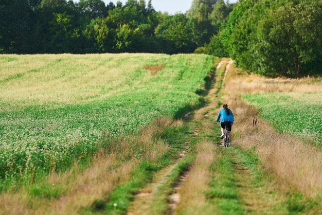 achteraanzicht van een jonge vrouw die op het platteland fietst en met de fiets buitenactiviteit reist