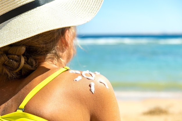 Achteraanzicht van een jonge vrouw die op het strand aan het looien is met zonnebrandcrème in de vorm van de zon op haar schouder. uv-bescherming tegen zonnebrand en zonnebrandcrème huidverzorgingsconcept