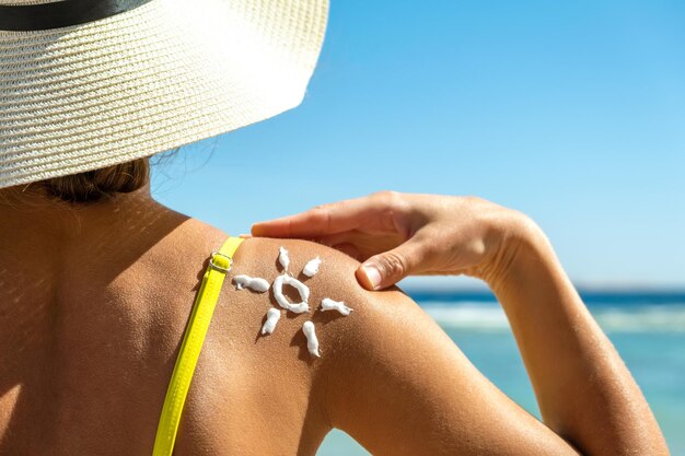 Achteraanzicht van een jonge vrouw die op het strand aan het looien is met zonnebrandcrème in de vorm van de zon op haar schouder. UV-bescherming tegen zonnebrand en zonnebrandcrème huidverzorgingsconcept