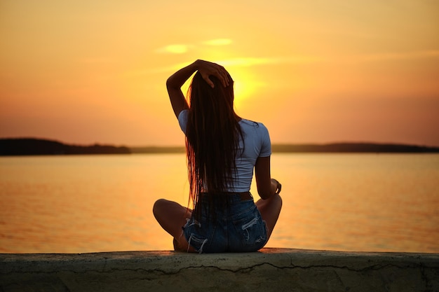 Achteraanzicht van een jonge vrouw die tijdens de zonsondergang op een pier zit