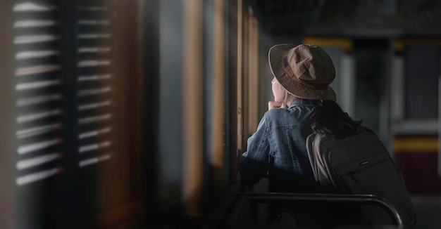 Achteraanzicht van een jonge vrouwelijke reiziger in een spijkerbroek die in de trein zit en wegkijkt buiten het raam