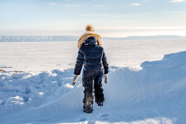 Achteraanzicht van een klein meisje alleen in het midden van een besneeuwde woestijn op een bevroren rivier