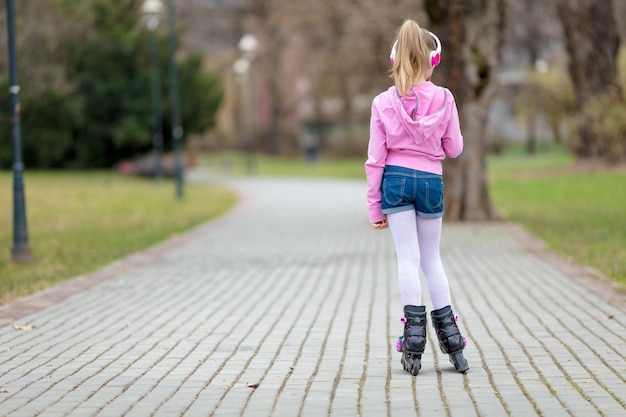 Achteraanzicht van een klein meisje inline skaten door het park.