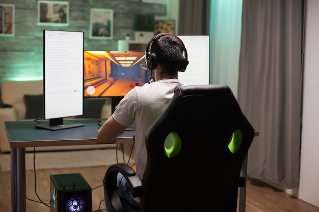 Achteraanzicht van een man die op een gamingstoel zit en 's nachts schietspel speelt. Neonlicht in de kamer.