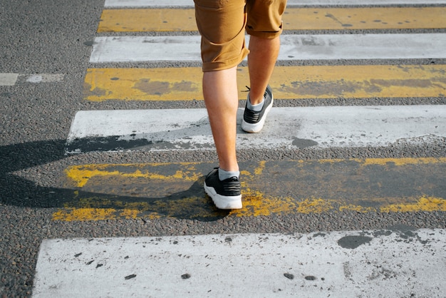 Achteraanzicht van een man in korte broek en sneakers die de weg oversteken op een zebrapad, close-up van mannelijke benen. Selectieve focus