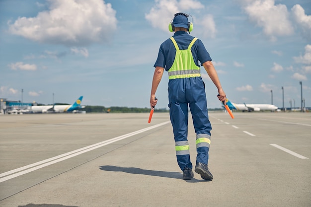 Achteraanzicht van een man in uniform en ruisonderdrukkende koptelefoon die naar de gelande vliegtuigen loopt