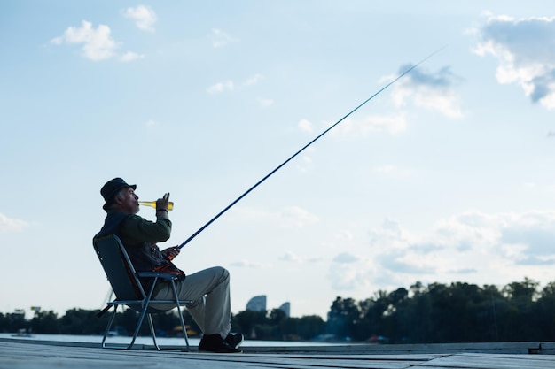 Achteraanzicht van een man met een hoed die zich vredig voelt terwijl hij vis vangt en bier drinkt