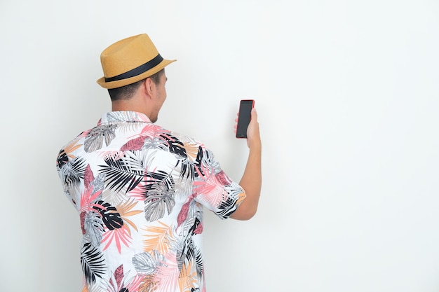 Achteraanzicht van een man met een strandshirt die naar zijn mobiele telefoon kijkt