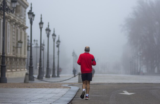 Achteraanzicht van een man met rood t-shirt die jogt in een mistige straat