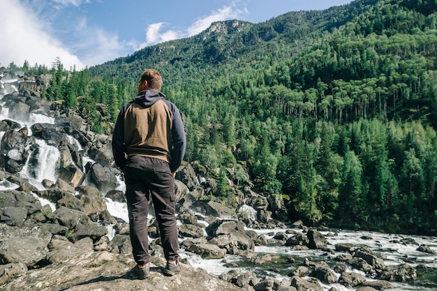 Achteraanzicht van een man tegen de achtergrond van een waterval en groene bergen