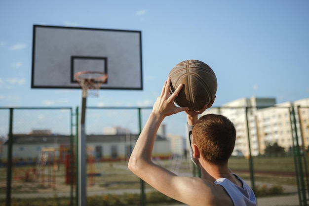 Achteraanzicht van een mannelijke basketballer die streetball speelt en in hoepel mikt tijdens training op de baan