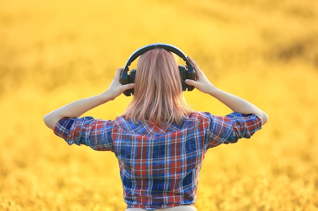 achteraanzicht van een meisje met een koptelefoon die naar muziek luistert in een bloemenveld, lentemuziek is gelukkig