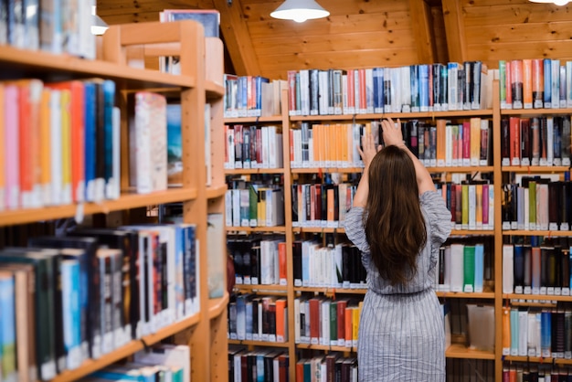 Achteraanzicht van een meisje met lang mooi horen staan in de buurt van boekenplanken