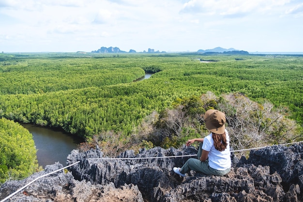 Achteraanzicht van een mooie jonge aziatische vrouw die op de bergtop zit terwijl ze door het mangrovebos reist