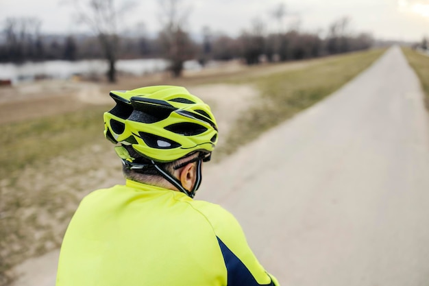 Achteraanzicht van een oudere fietser die op een fiets in de natuur rijdt