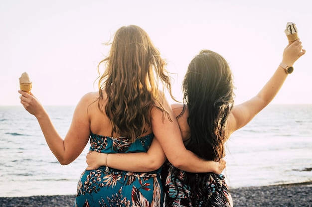 Achteraanzicht van een paar vrouwelijke vrienden knuffelen en genieten samen van de zomer terwijl ze een ijsje eten