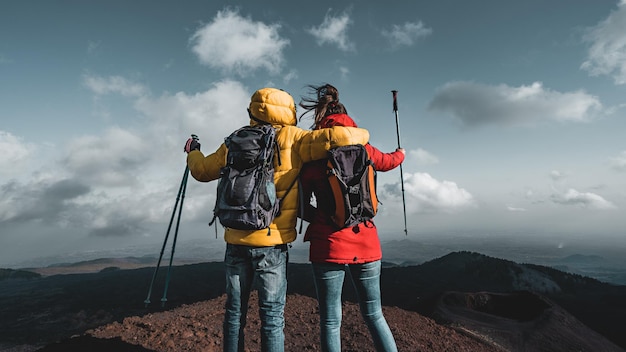 Achteraanzicht van een paar wandelaars met rugzak en palen kijken naar het panorama vanaf de top van de Etna op Sicilië, Italië, de grote Europese actieve vulkaan