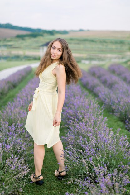 Achteraanzicht van een prachtig jong meisje in een lichtgele jurk die geniet van een wandeling in een lavendelveld in de zomer