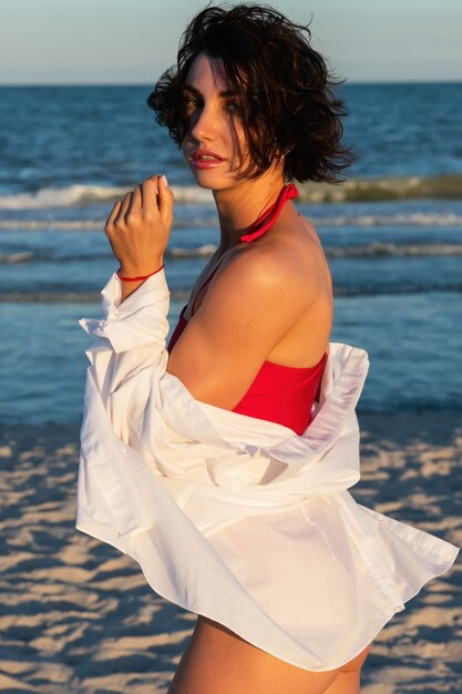 Achteraanzicht van een sexy getatoeëerd jong meisje in een rode zwembroek poseren op het strand. Mooie blonde vrouw met lang haar ontspant door de oceaan. Het concept van een sportmodel, badkleding