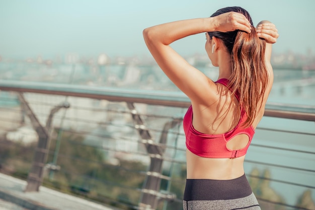 Achteraanzicht van een sportieve vrouw die op de brug staat en een paardenstaart maakt voor de training