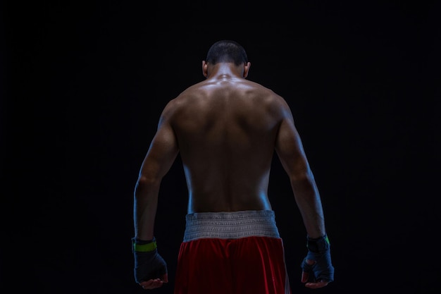 Achteraanzicht van een sterk jong mannelijk bokser fitness mannelijk model met bokshandschoenen op een zwarte rug...