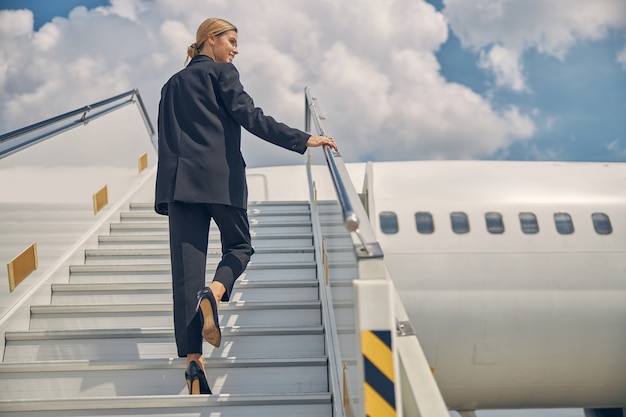 Achteraanzicht van een tevreden jonge blanke vrouwelijke luchthavenmedewerker die de passagierstrap oploopt