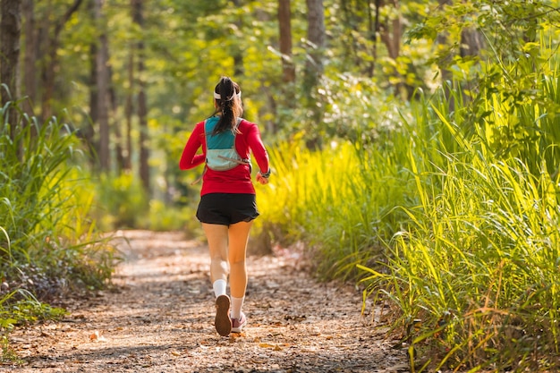 Achteraanzicht van een volwassen Aziatische trailrunner met hardloopvest beoefent trailrunning in het bos