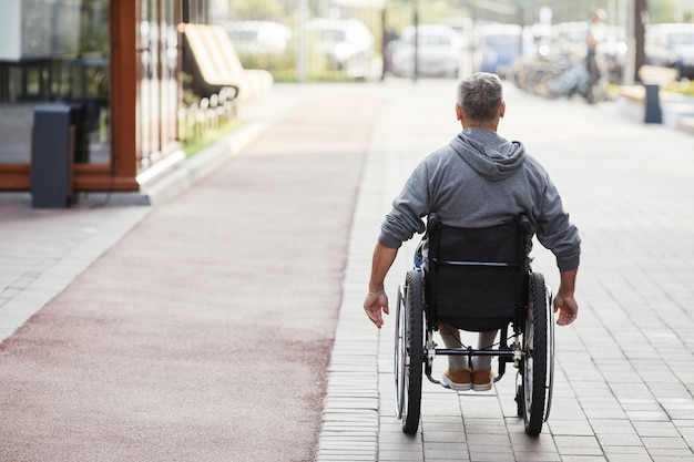 Achteraanzicht van een volwassen man met een handicap die in een rolstoel langs de straat rijdt